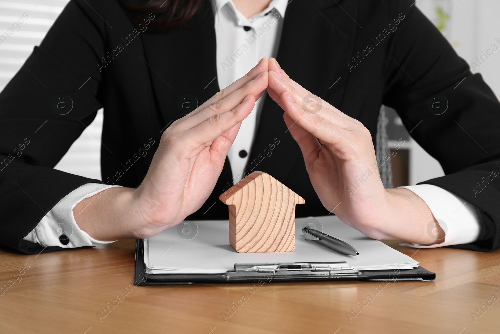 Photo of Property insurance. Real estate agent protecting wooden house figure at table indoors, closeup