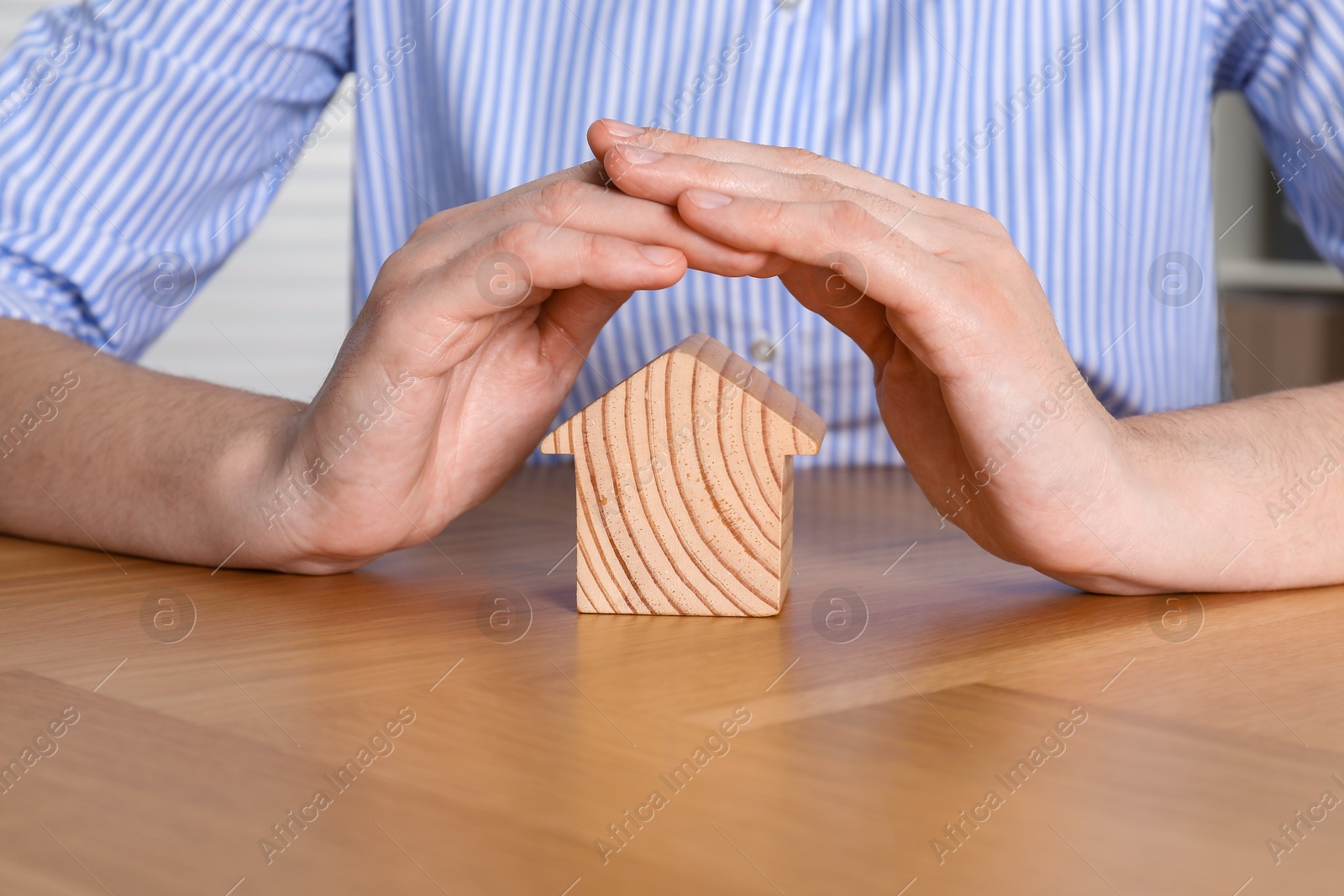 Photo of Property insurance. Real estate agent protecting wooden house figure at table indoors, closeup