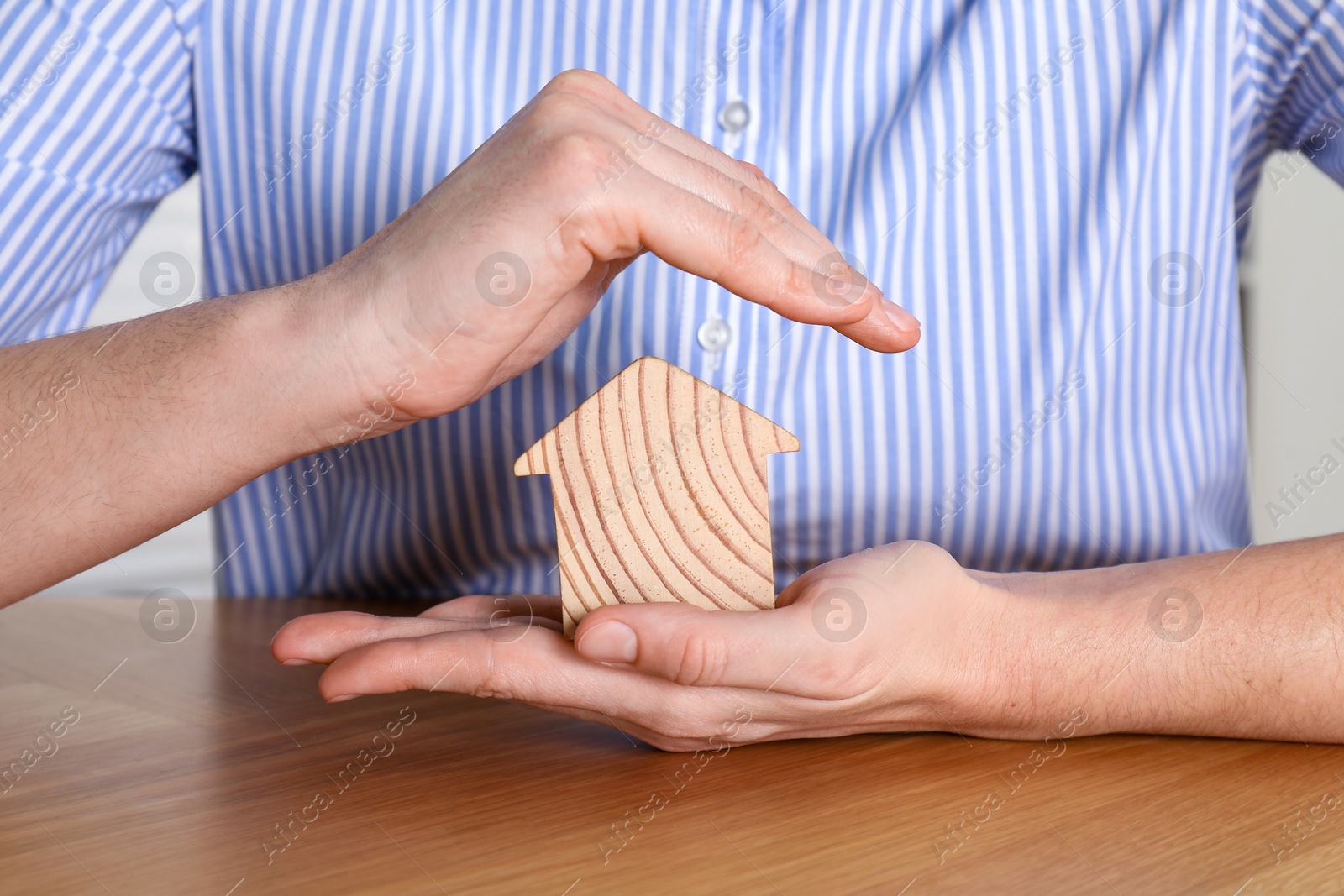 Photo of Property insurance. Real estate agent protecting wooden house figure at table indoors, closeup