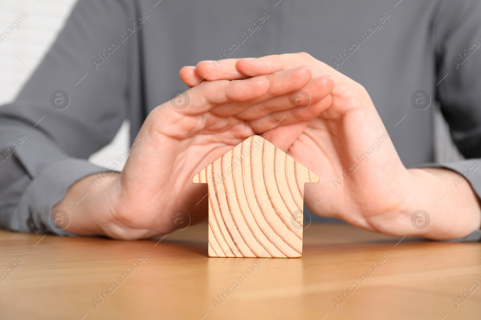 Photo of Property insurance. Real estate agent protecting wooden house figure at table indoors, closeup