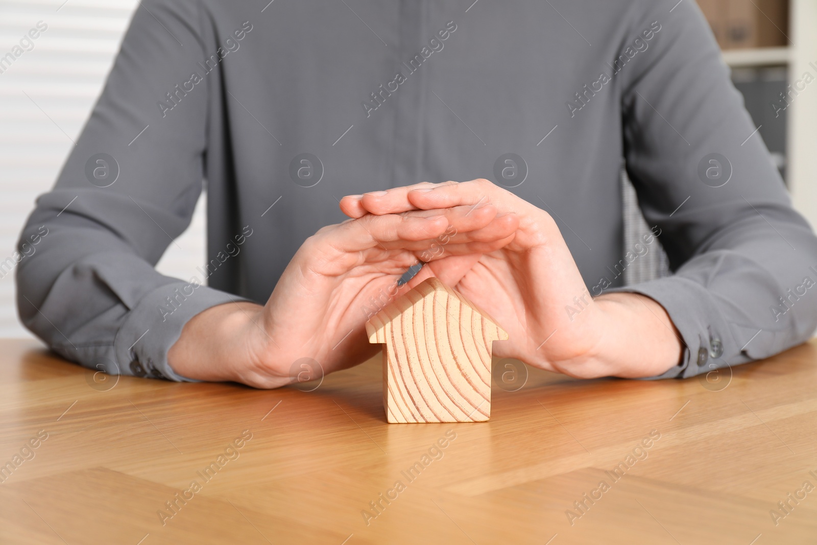 Photo of Property insurance. Real estate agent protecting wooden house figure at table indoors, closeup