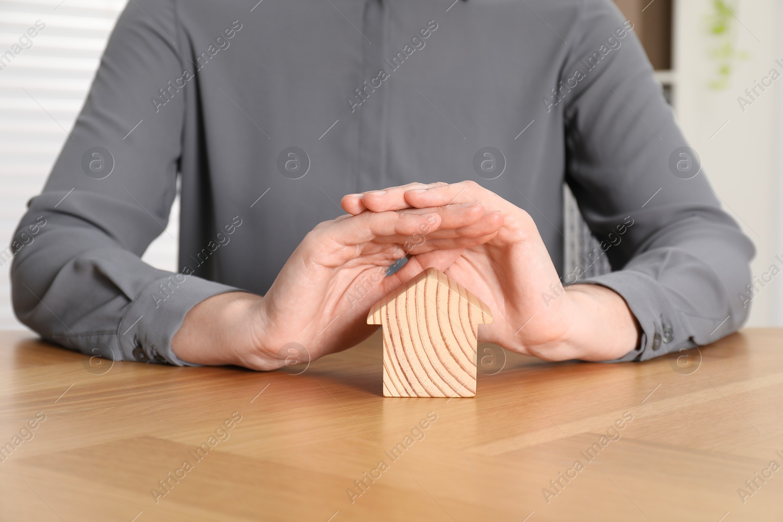 Photo of Property insurance. Real estate agent protecting wooden house figure at table indoors, closeup