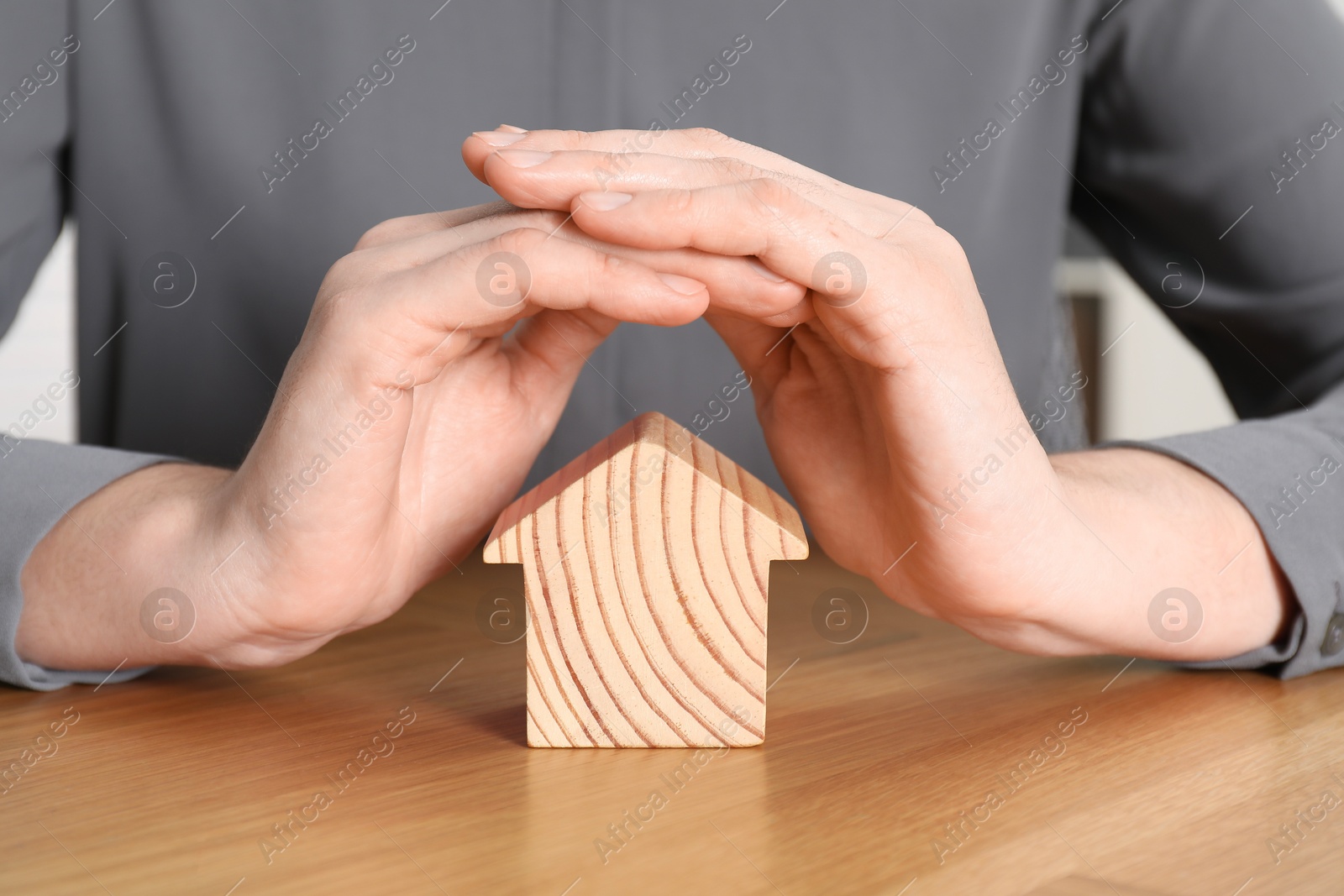 Photo of Property insurance. Real estate agent protecting wooden house figure at table indoors, closeup