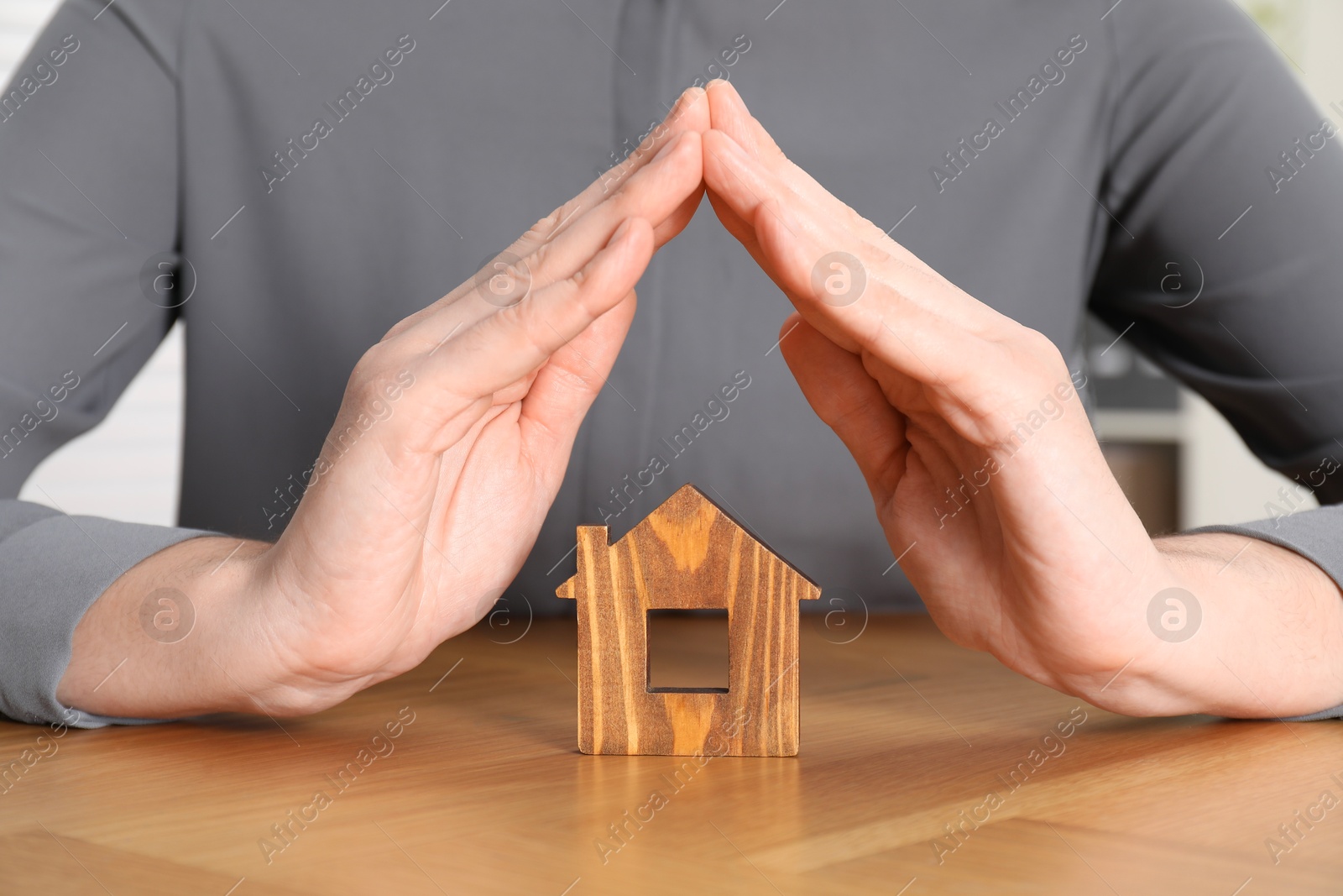 Photo of Property insurance. Real estate agent protecting wooden house figure at table indoors, closeup