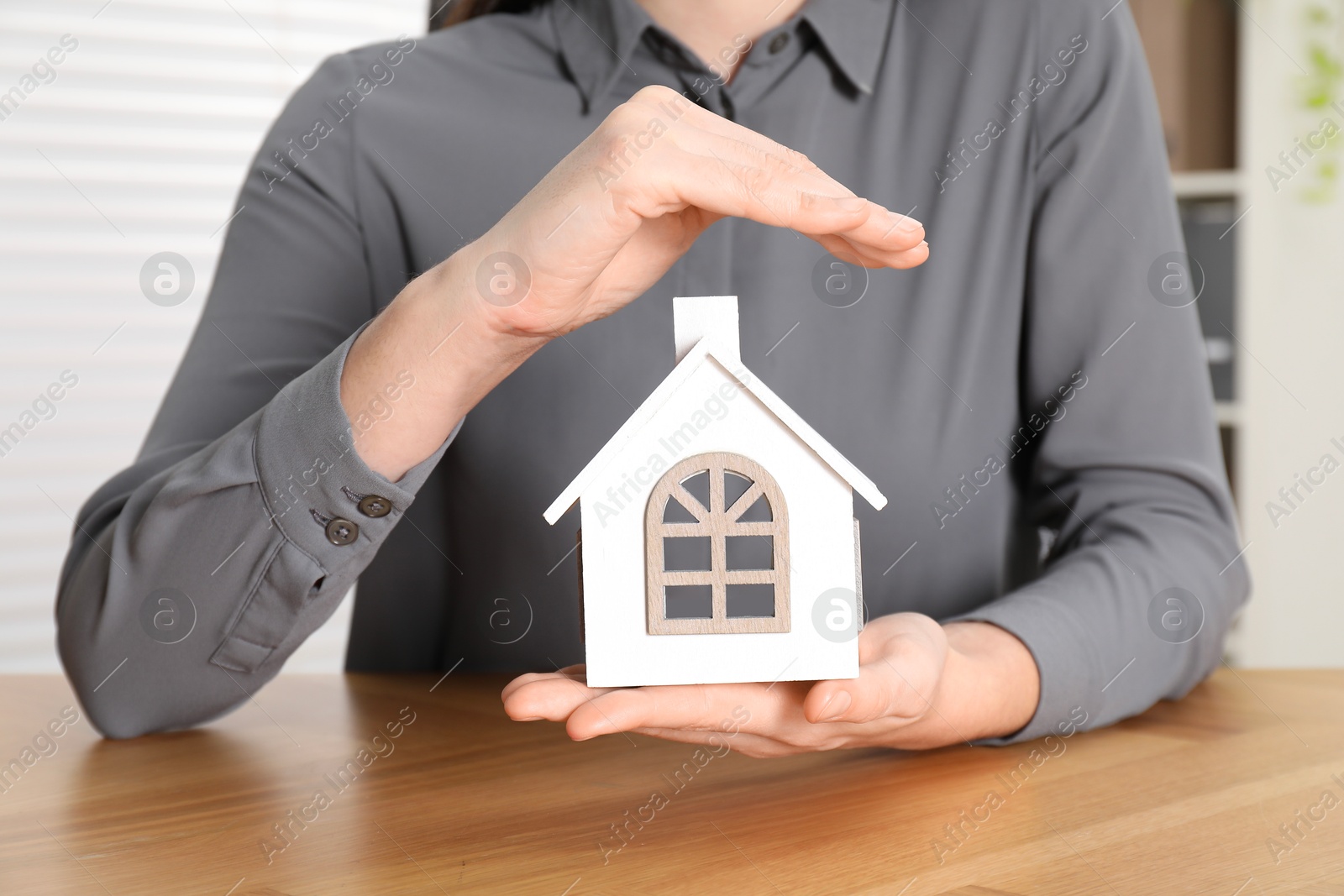 Photo of Property insurance. Real estate agent protecting house figure at wooden table indoors, closeup