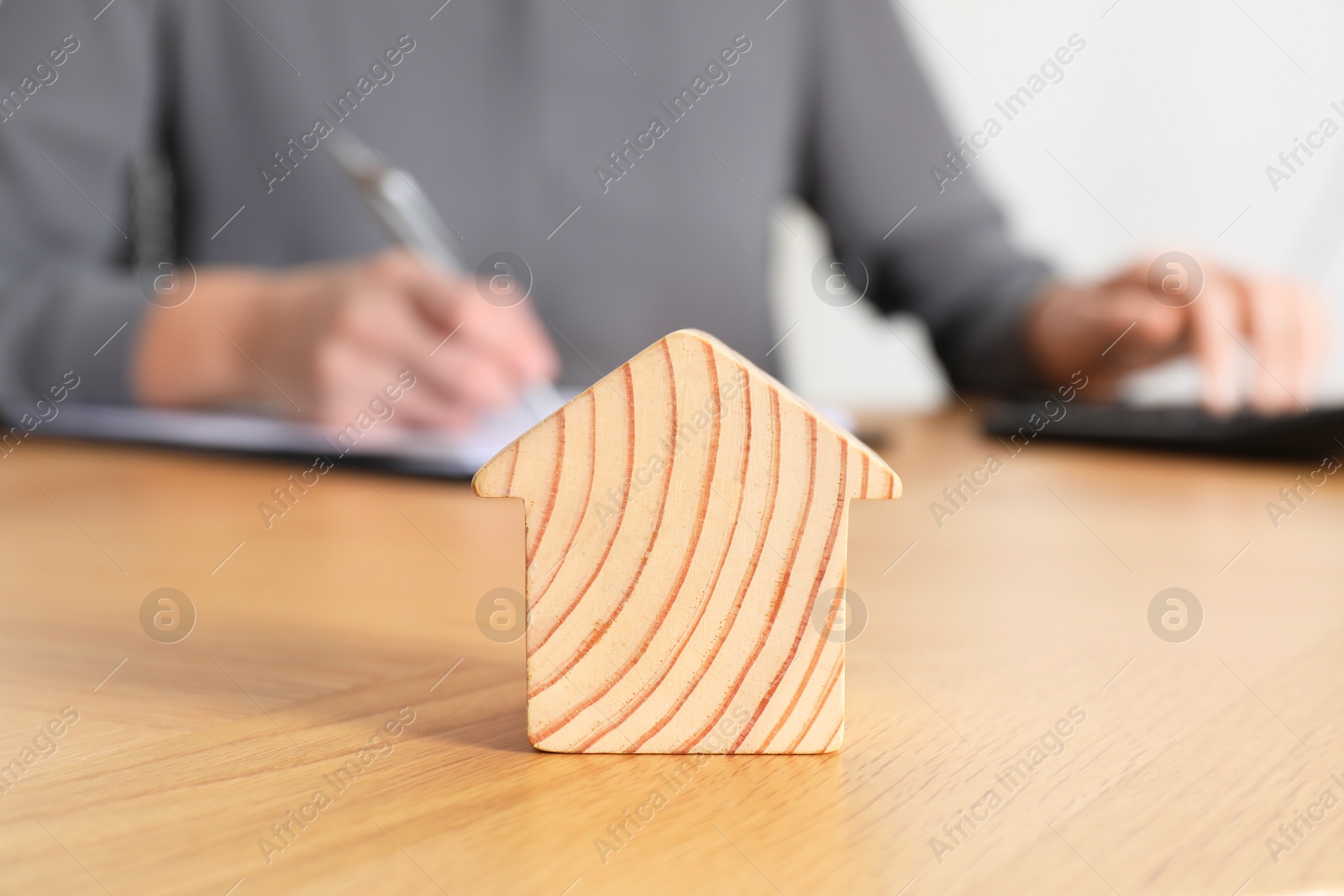 Photo of Property insurance. Real estate agent working at table indoors, focus on wooden house figure