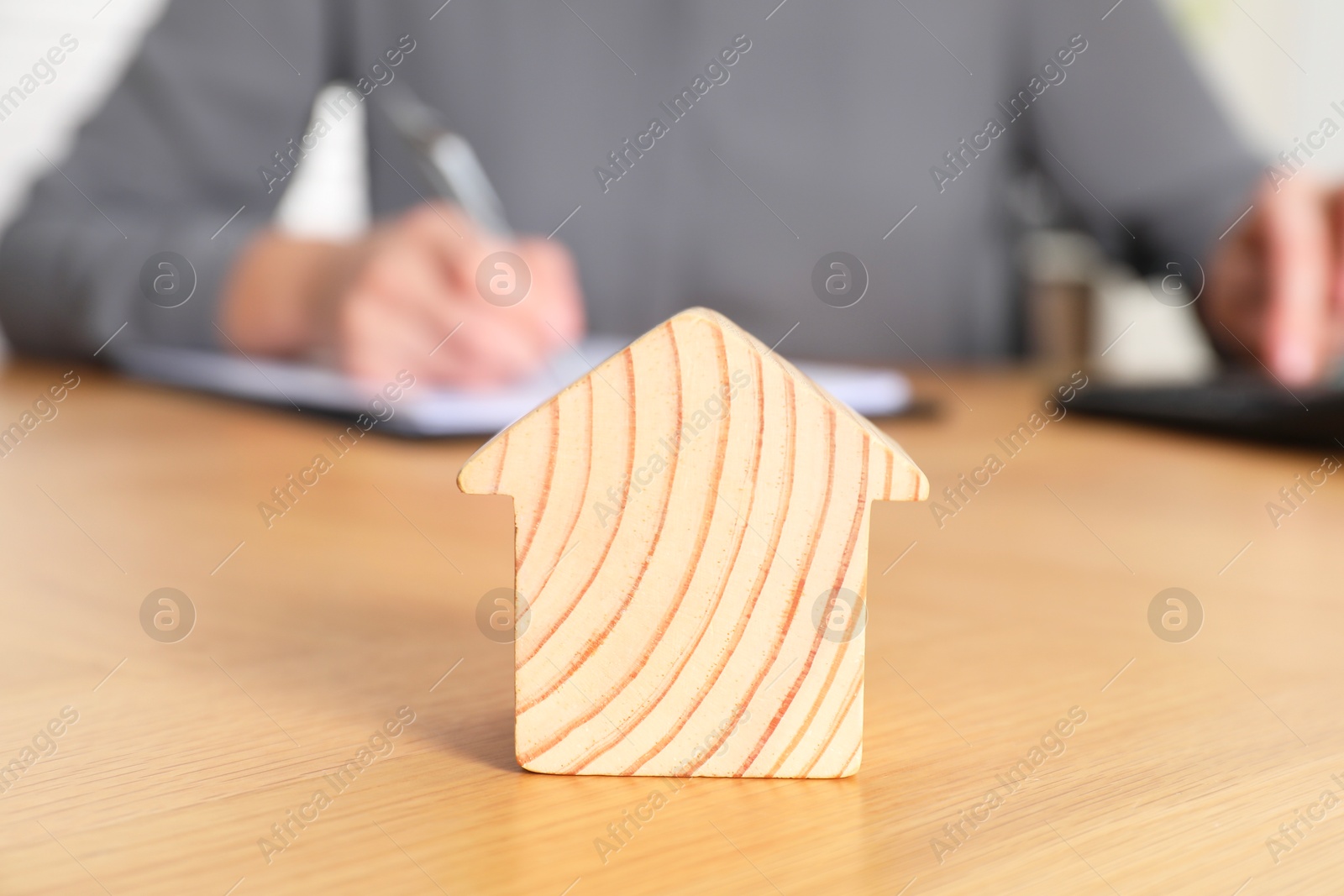 Photo of Property insurance. Real estate agent working at table indoors, focus on wooden house figure