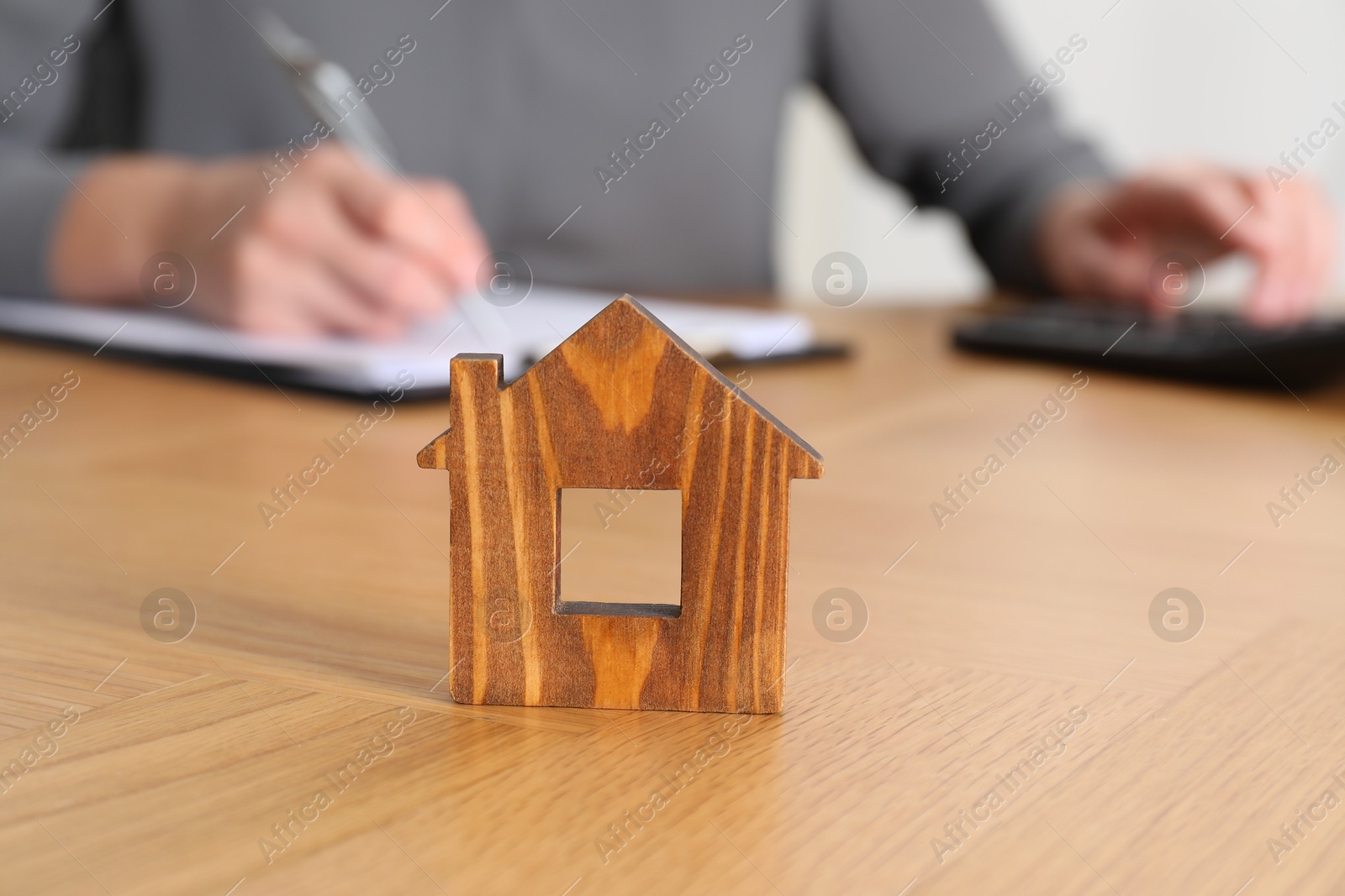 Photo of Property insurance. Real estate agent working at table indoors, focus on wooden house figure