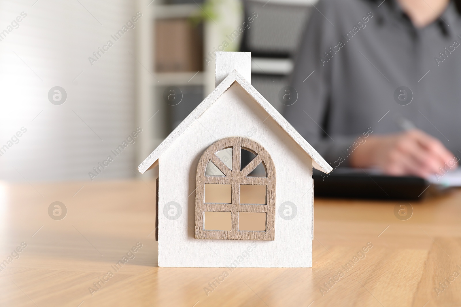 Photo of Property insurance. Real estate agent working at wooden table indoors, focus on house figure