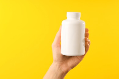 Photo of Woman holding medical bottle with pills on yellow background, closeup. Space for text