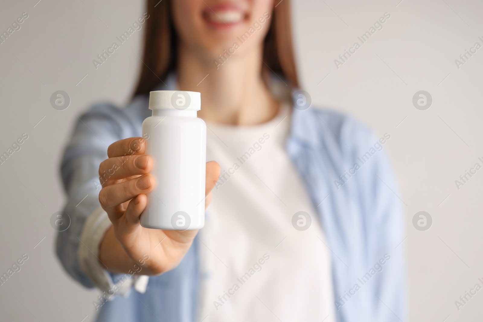 Photo of Woman holding medical bottle with pills on light background, closeup