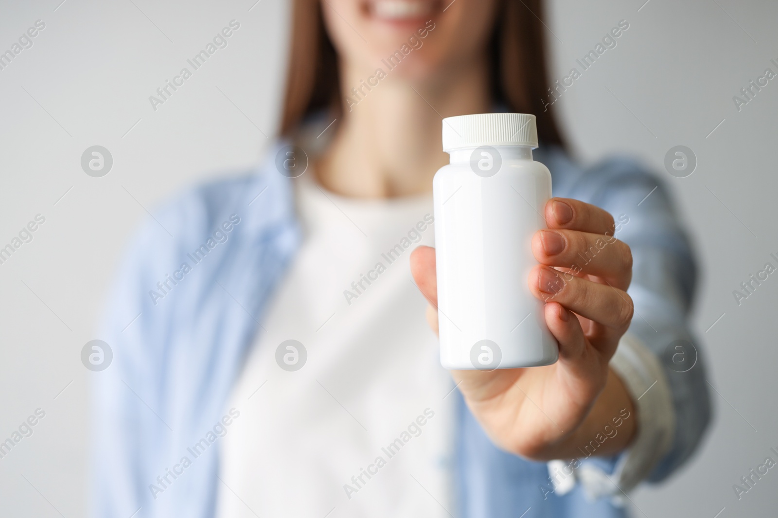 Photo of Woman holding medical bottle with pills on light background, closeup