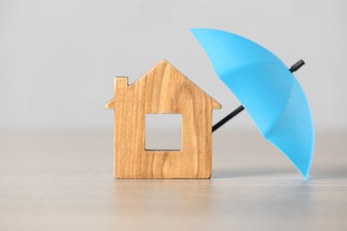 Photo of Property insurance. Wooden house figure and small umbrella on table