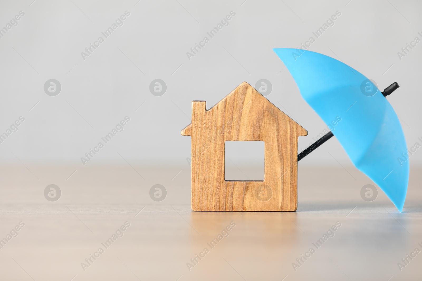 Photo of Property insurance. Wooden house figure and small umbrella on table, space for text