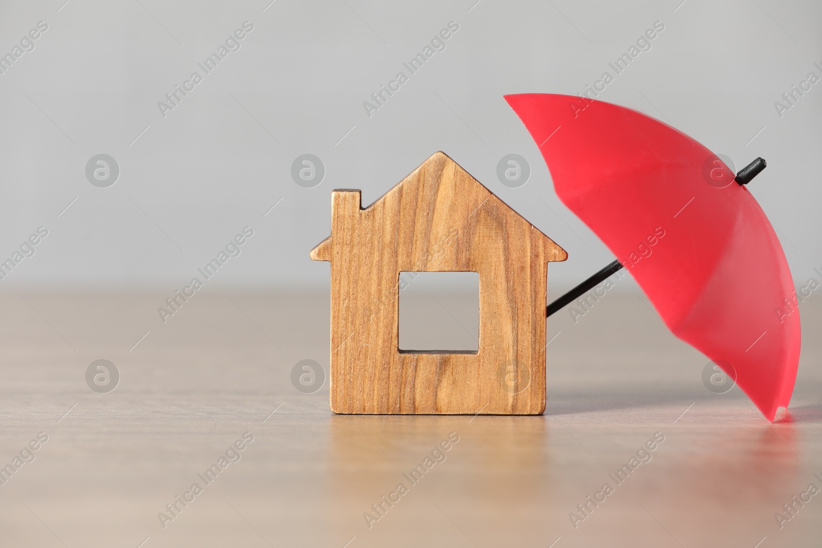 Photo of Property insurance. Wooden house figure and small umbrella on table, space for text