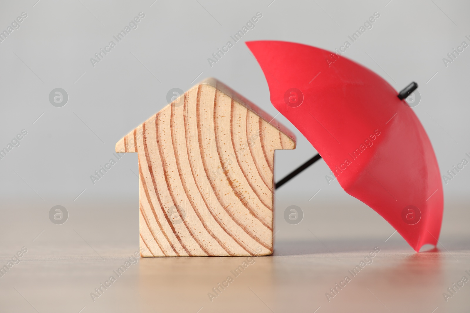 Photo of Property insurance. Wooden house figure and small umbrella on table