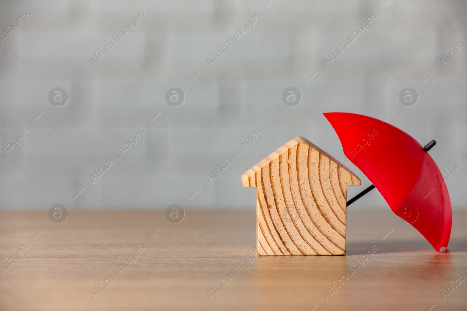 Photo of Property insurance. Wooden house figure and small umbrella on table, space for text