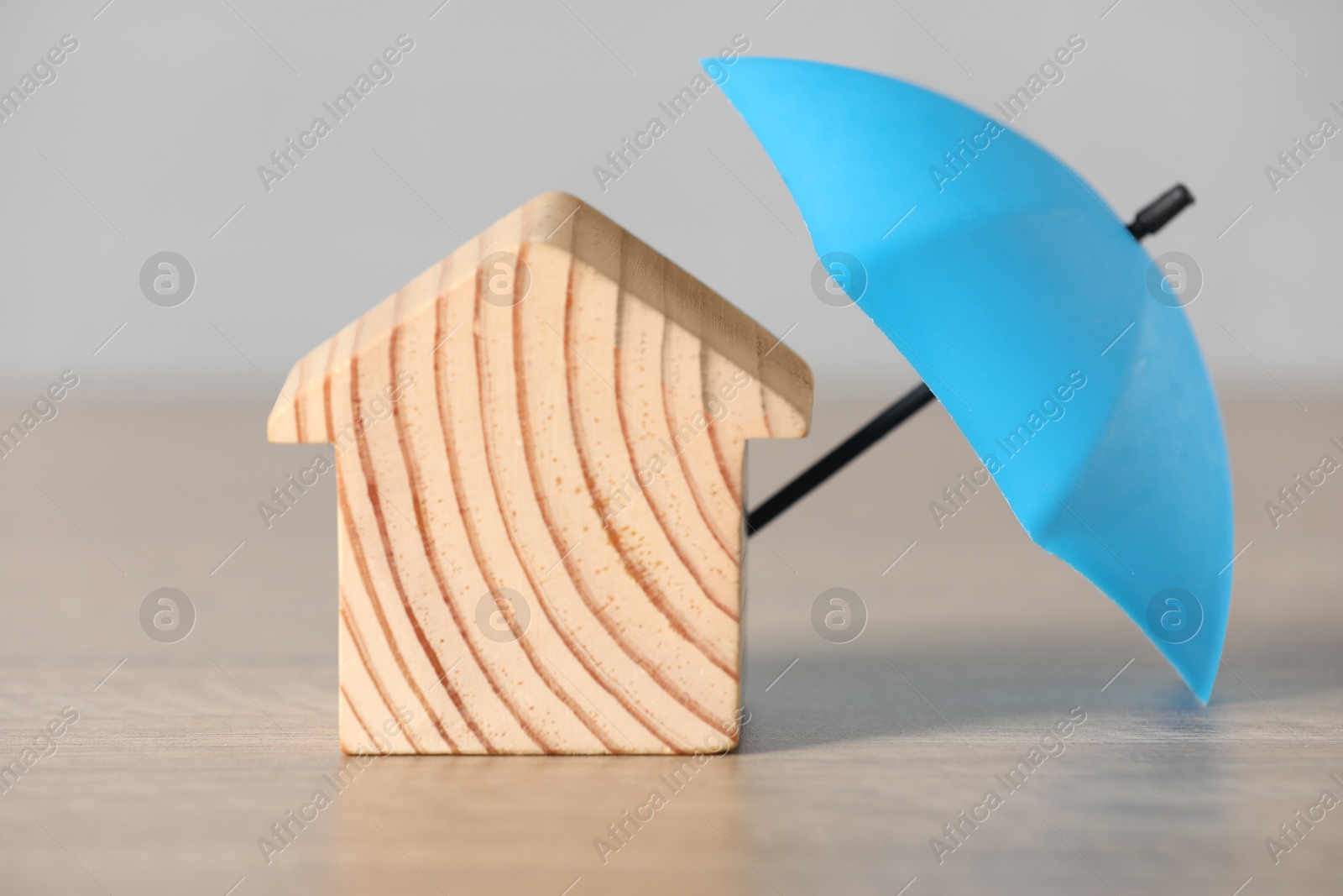 Photo of Property insurance. Wooden house figure and small umbrella on table