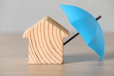 Photo of Property insurance. Wooden house figure and small umbrella on table