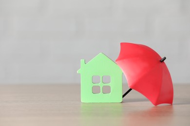 Photo of Property insurance. House figure and small umbrella on table, space for text