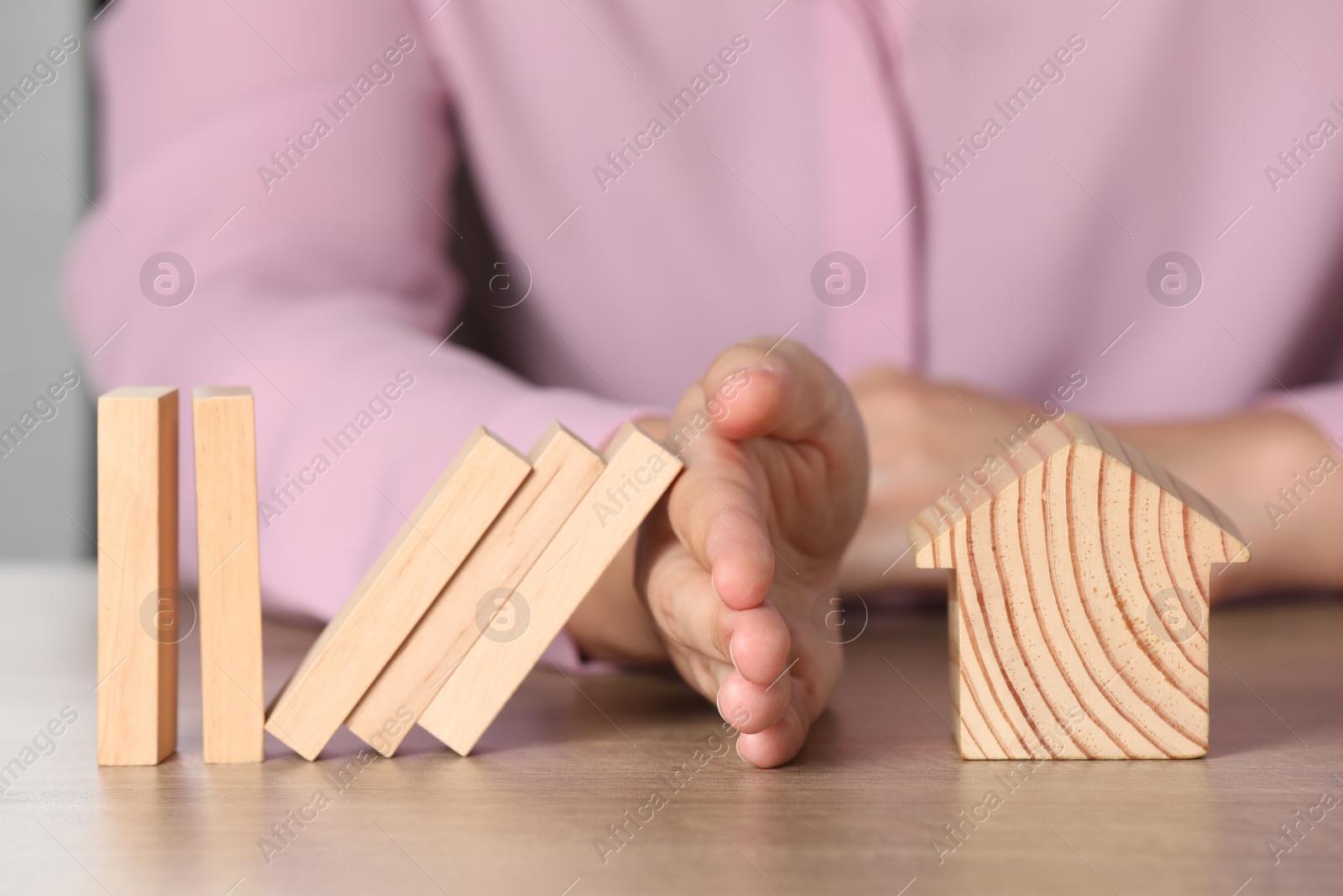 Photo of Property insurance. Real estate agent protecting wooden house figure at table indoors, closeup