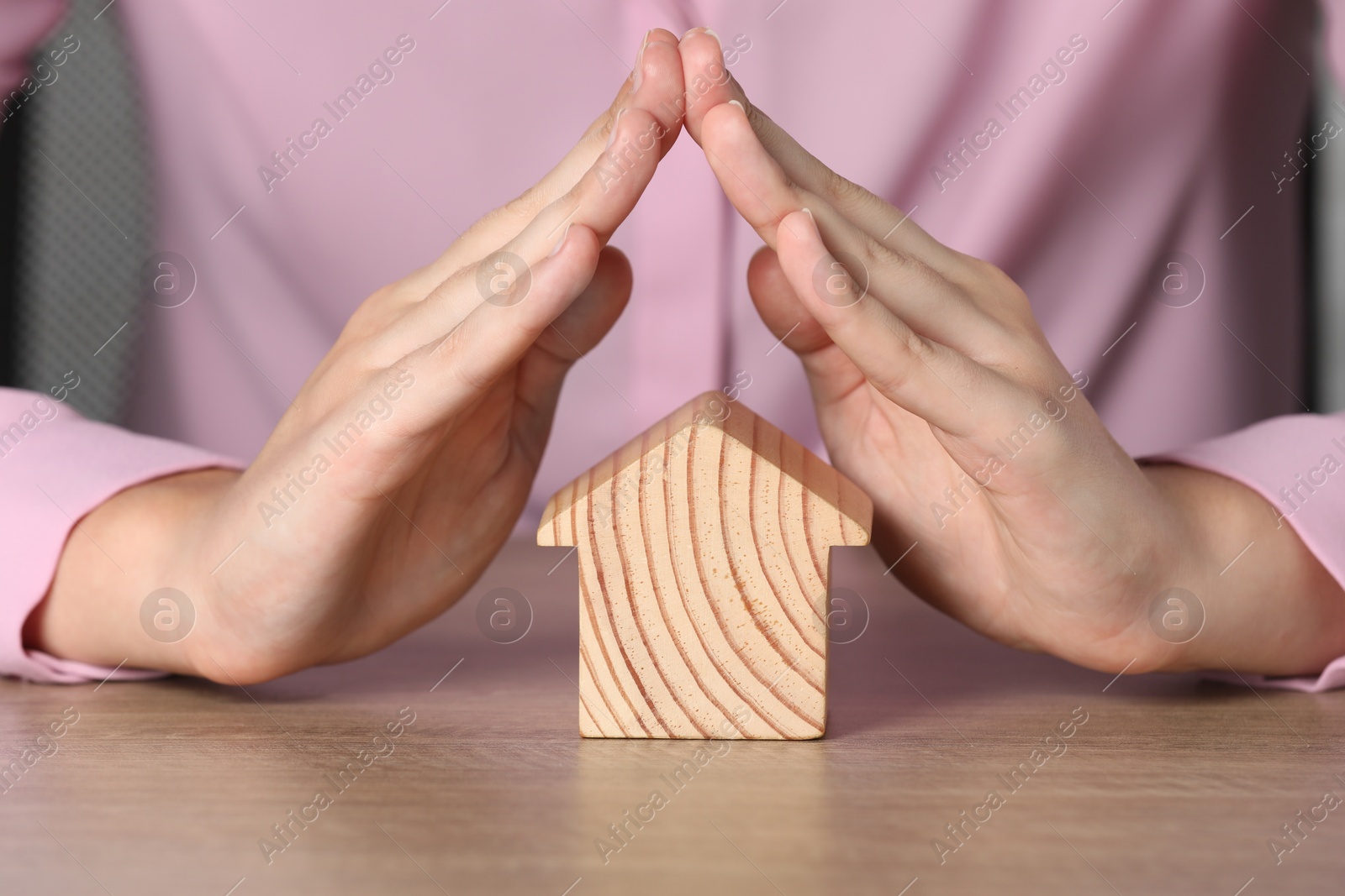 Photo of Property insurance. Real estate agent protecting wooden house figure at table indoors, closeup