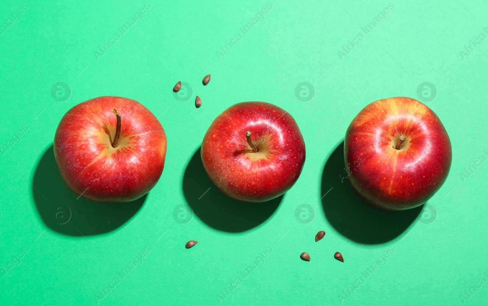 Photo of Red apples and seeds on green background, flat lay