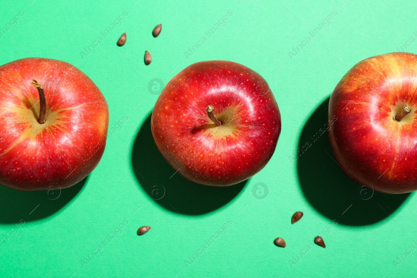 Photo of Red apples and seeds on green background, flat lay