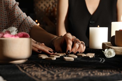 Photo of Fortuneteller with wooden runes reading woman's future at divination mat, closeup