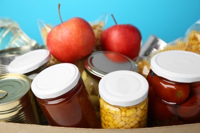 Photo of Different food products for donation in box on light blue background, closeup