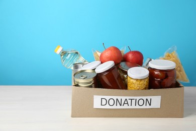 Photo of Different food products for donation in box on table against light blue background, space for text