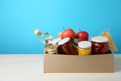 Photo of Different food products for donation in box on table against light blue background, space for text