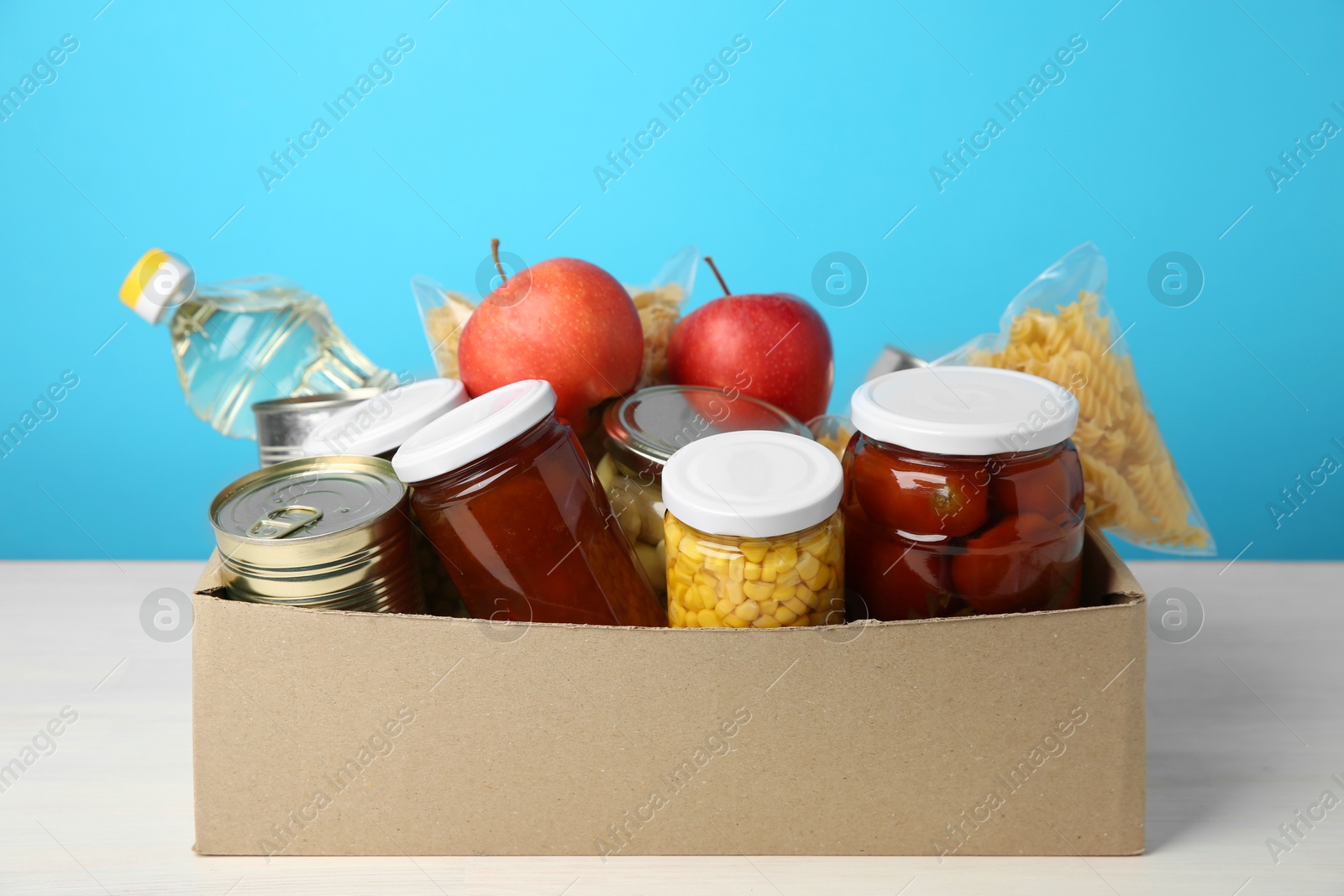 Photo of Different food products for donation in box on table against light blue background