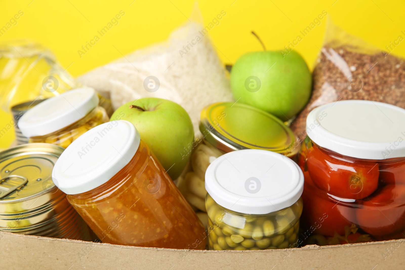 Photo of Different food products for donation in box on yellow background, closeup