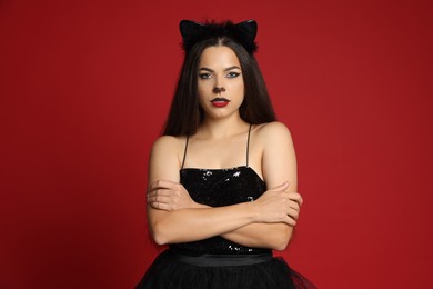 Photo of Woman with cat makeup and ears in beautiful dress on red background