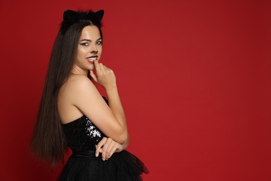 Photo of Woman with cat makeup and ears in beautiful dress on red background. Space for text