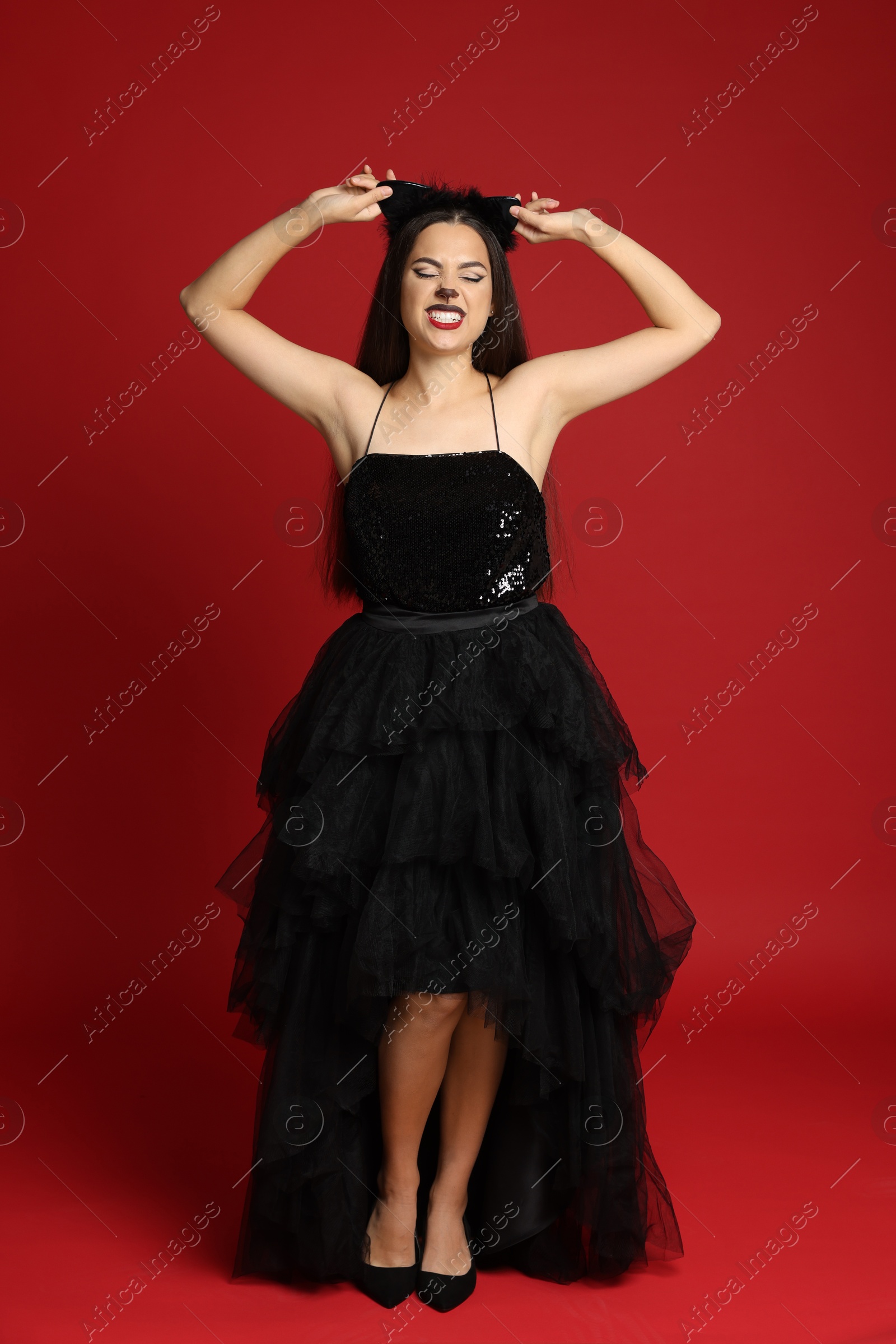 Photo of Woman with cat makeup and ears in beautiful dress on red background