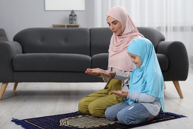 Photo of Muslim woman and her daughter praying on mat at home