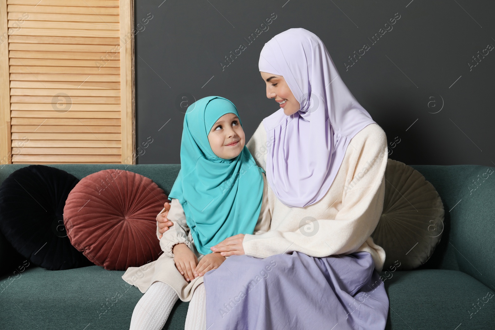 Photo of Muslim woman and her daughter sitting on sofa at home