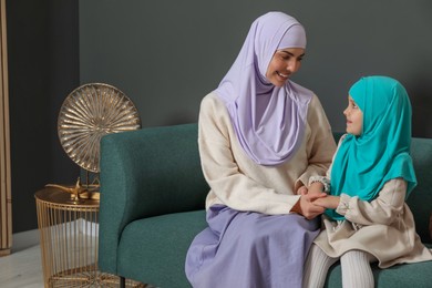 Photo of Muslim woman and her daughter sitting on sofa at home