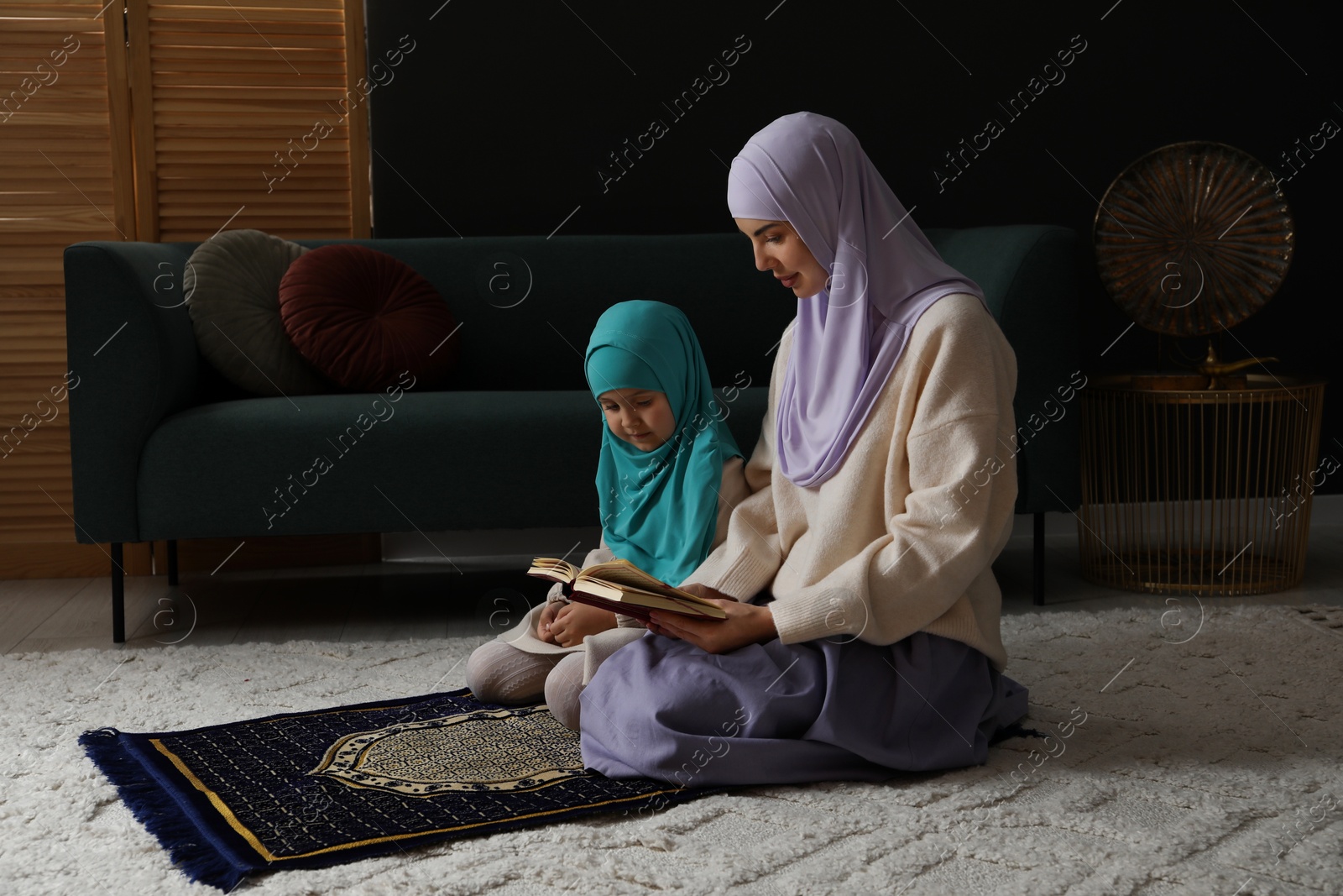 Photo of Muslim woman and her daughter with Quran praying on mat at home