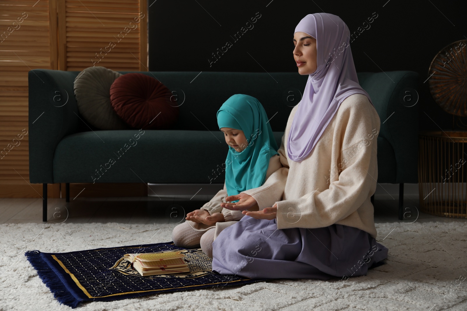 Photo of Muslim woman and her daughter with Quran praying on mat at home