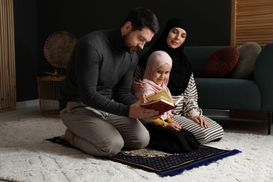 Photo of Muslim family with Quran praying on mat at home