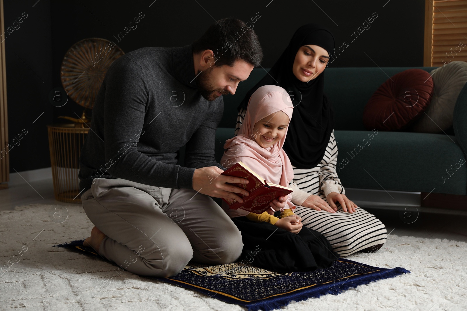 Photo of Muslim family with Quran praying on mat at home