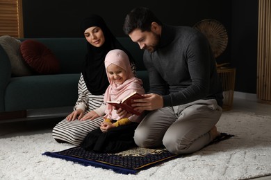 Photo of Muslim family with Quran praying on mat at home