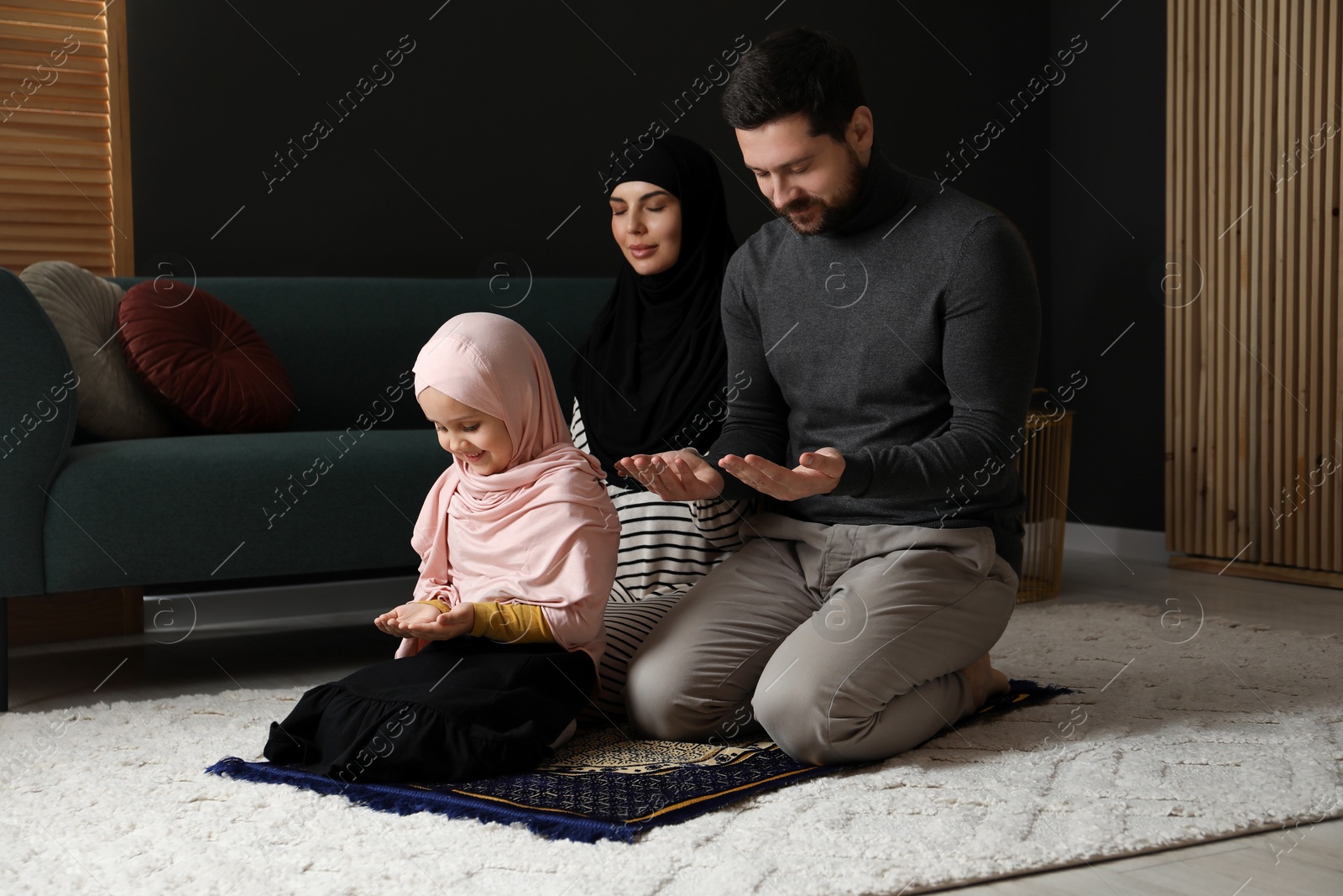 Photo of Muslim family praying on mat at home