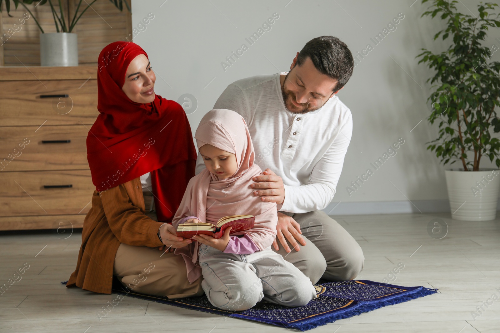 Photo of Muslim family with Quran praying on mat at home