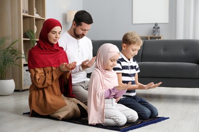 Photo of Happy Muslim family praying on mat at home