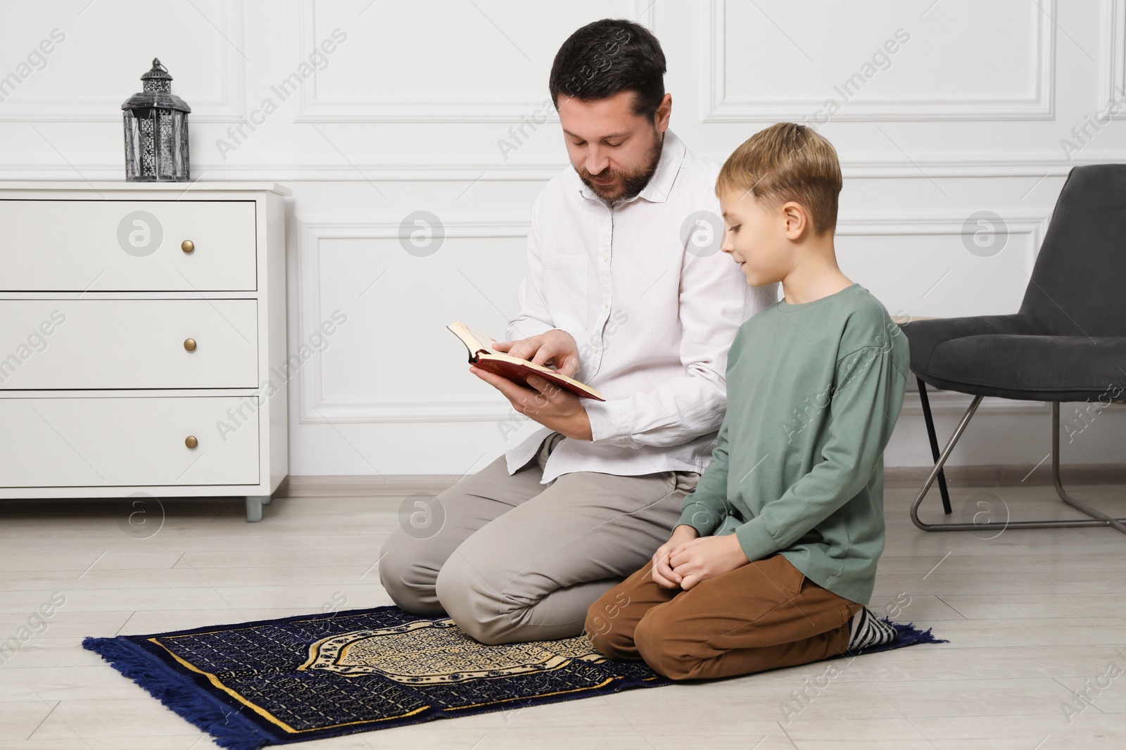 Photo of Muslim man and his son with Quran praying on mat at home