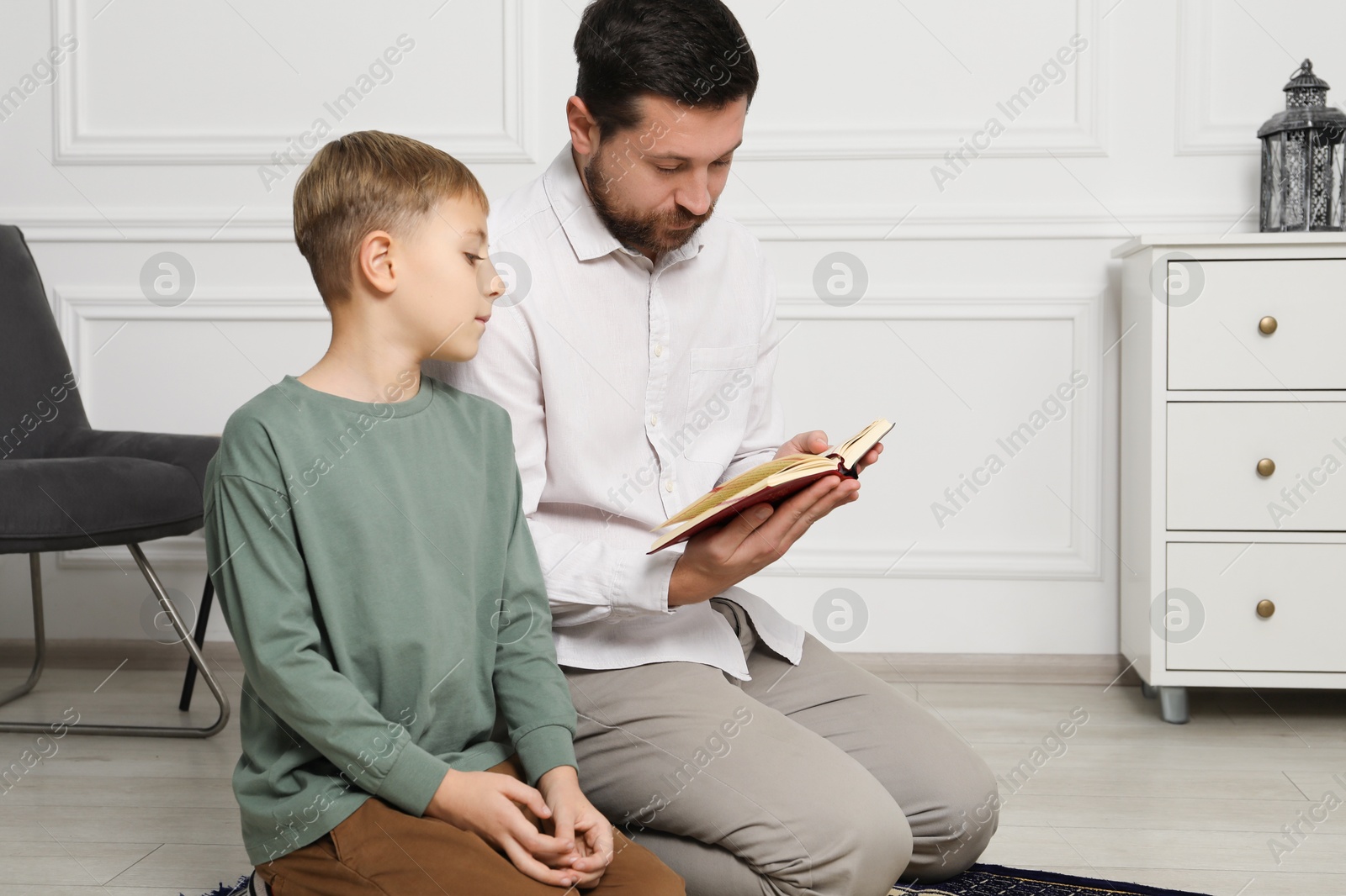 Photo of Muslim man and his son with Quran praying on mat at home